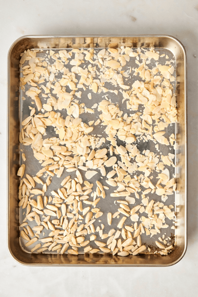 Amandes tranchées et émondées étalées uniformément sur une plaque de cuisson en métal.