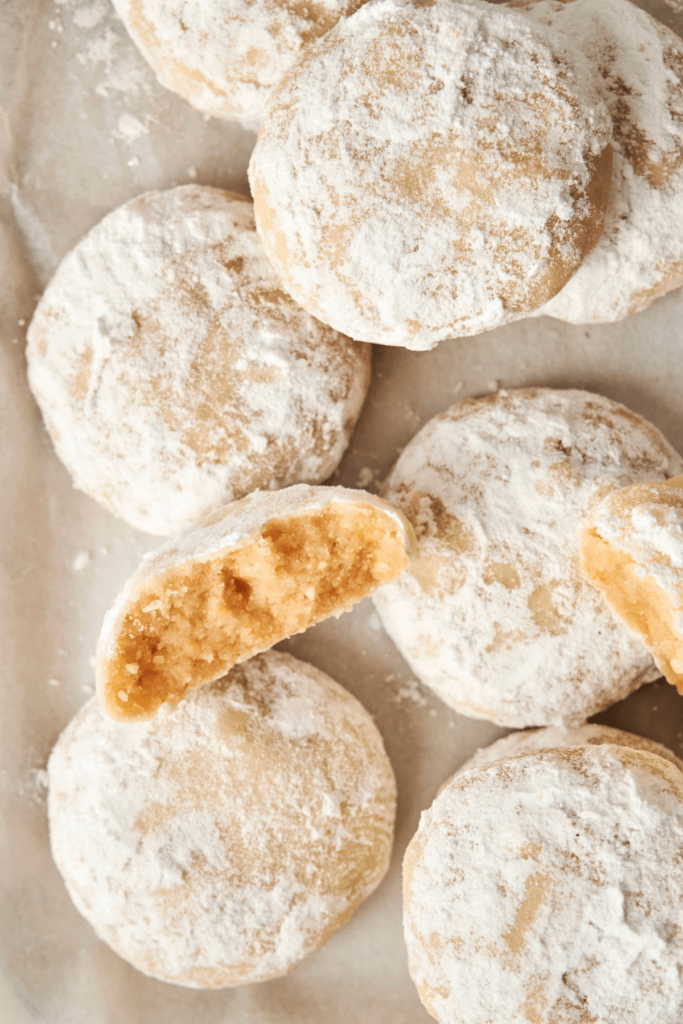 Gros plan sur des Biscuits Boule Neige aux Amandes enrobés de sucre glace, avec un biscuit cassé en deux pour dévoiler son intérieur doux et friable.