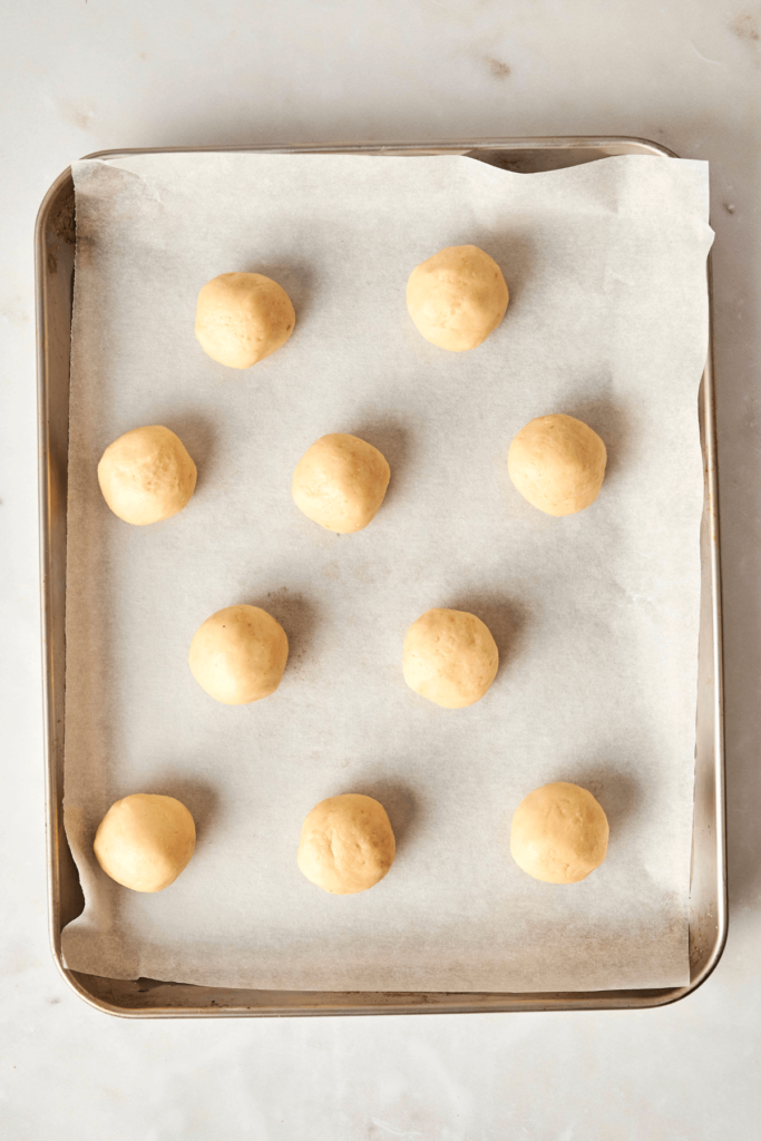 Plaque de cuisson tapissée de papier sulfurisé avec des boules de pâte à biscuits aux amandes disposées uniformément.