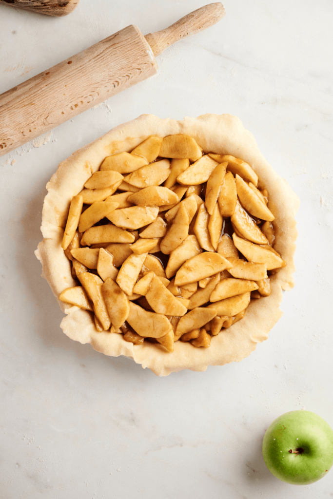 Garniture de tarte aux pommes superposée dans une croûte de tarte non cuite, prête à être recouverte et cuite.