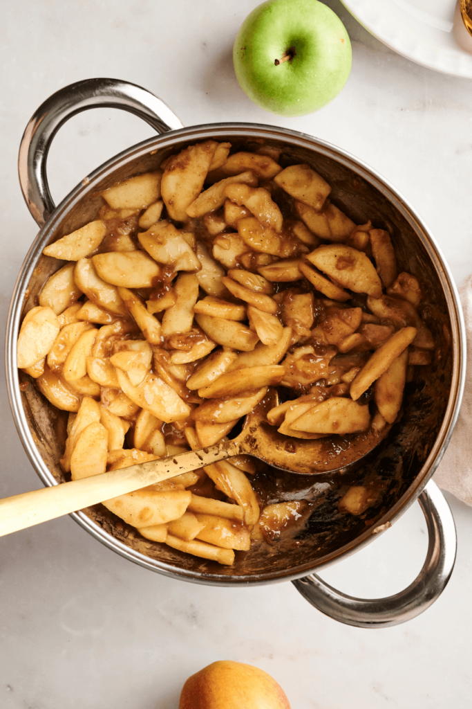 Garniture de tarte aux pommes cuite avec des tranches de pommes tendres aux épices de cannelle dans une casserole, prête à être ajoutée à une croûte de tarte feuilletée pour la cuisson.