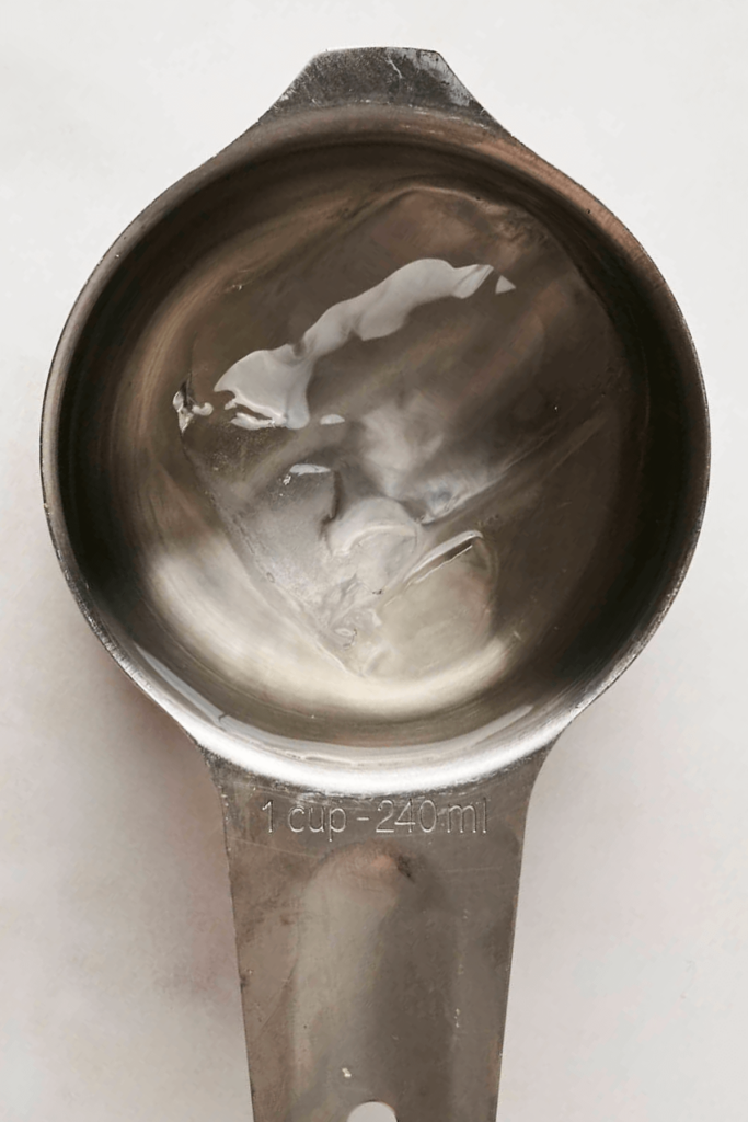 Close-up of a measuring cup filled with ice water and white vinegar.