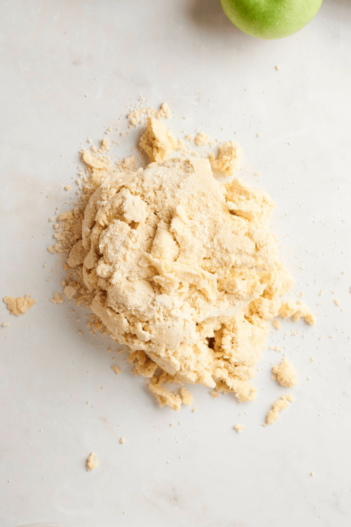 Roughly combined pie dough placed on a floured surface, ready to be kneaded and shaped for pie crust.