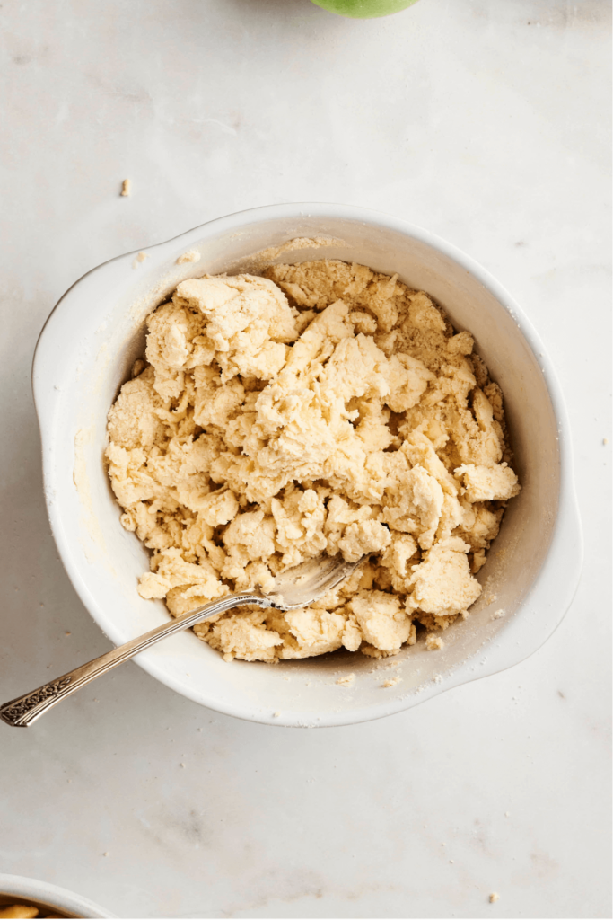 Bowl of pie dough coming together with a spoon, showing the texture of pie crust dough.