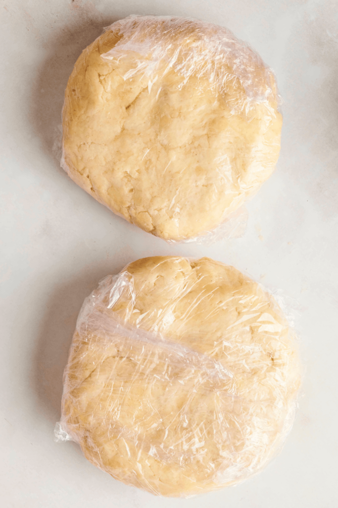Two discs of homemade pie dough wrapped in plastic wrap, ready to be chilled for flaky crusts.