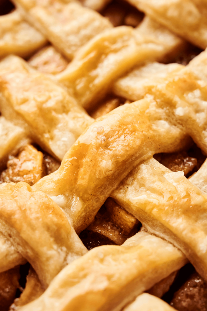 Detailed close-up of a golden, flaky lattice pie crust with visible caramelized sugar and apple filling beneath.