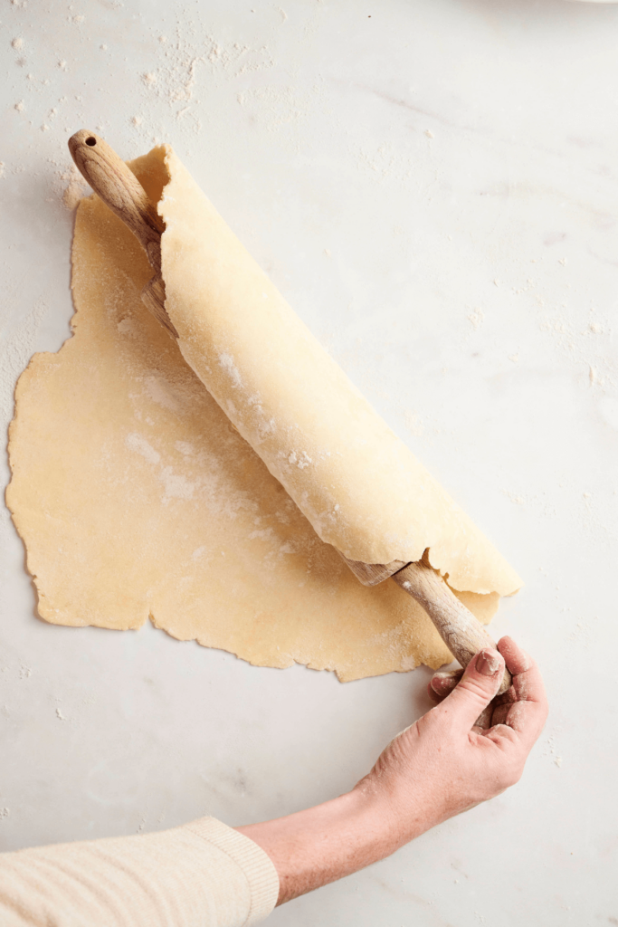 Pie dough wrapped around a rolling pin, ready to be transferred to a pie dish.
