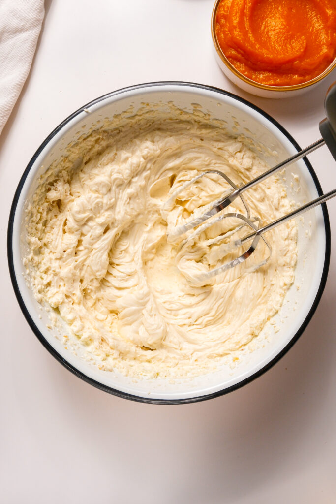 Bol de fromage à la crème et de sucres en cours de mélange avec un batteur à main jusqu'à obtenir une consistance mousseuse pour la base d'une garniture crémeuse de cheesecake à la citrouille.