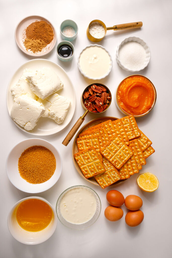 Vue de dessus de tous les ingrédients nécessaires pour un cheesecake à la citrouille, y compris le fromage à la crème, la purée de citrouille, le sucre brun et les épices.