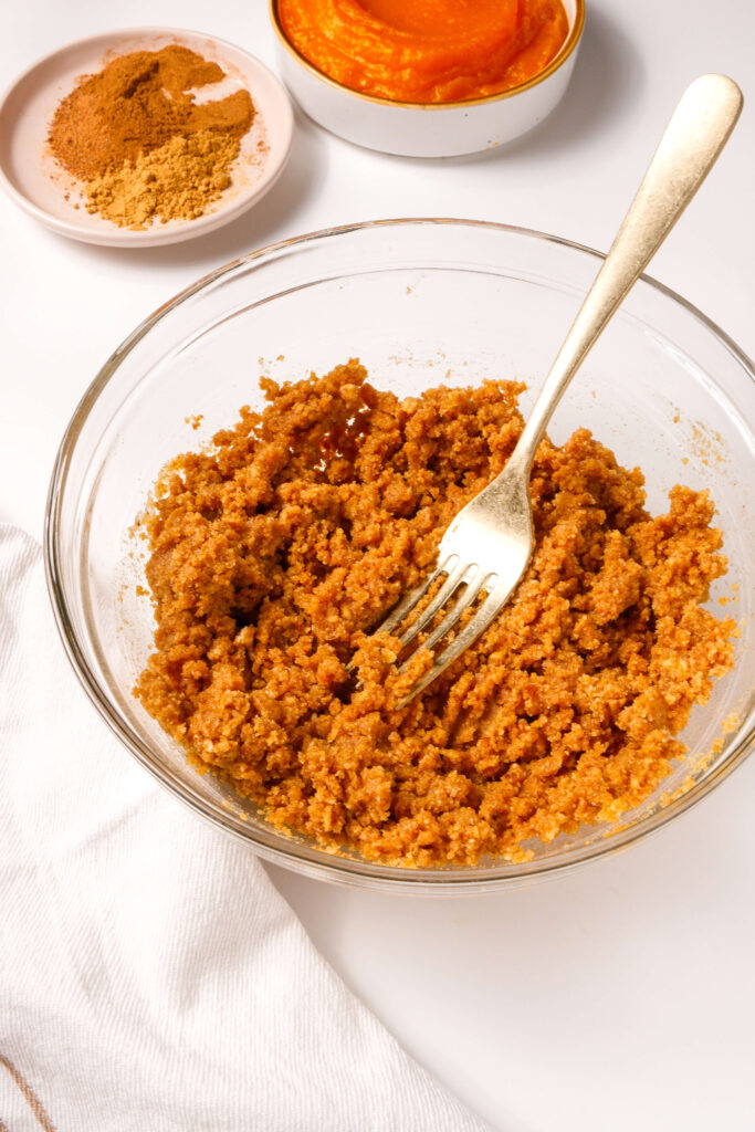 Bol de mélange de miettes de biscuit graham, de noix de pécan et de beurre prêt à être pressé dans une croûte pour un cheesecake à la citrouille.