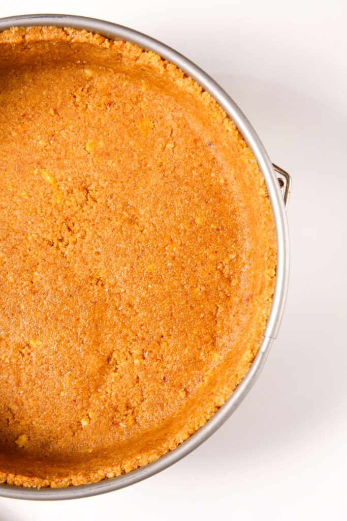Gros plan sur une croûte de biscuit graham et de noix de pécan parfaitement pressée dans un moule à charnière, prête pour la garniture du cheesecake à la citrouille.