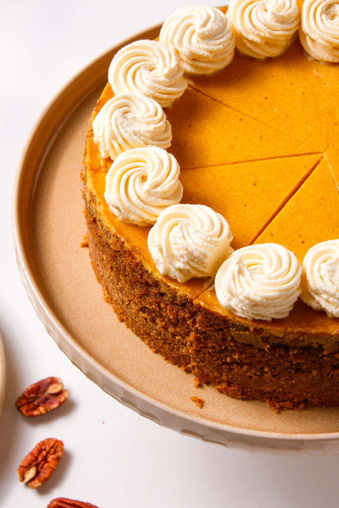Gros plan sur un cheesecake à la citrouille tranché, surmonté de tourbillons de crème fouettée à la cannelle, mettant en valeur la croûte détaillée et la texture lisse.