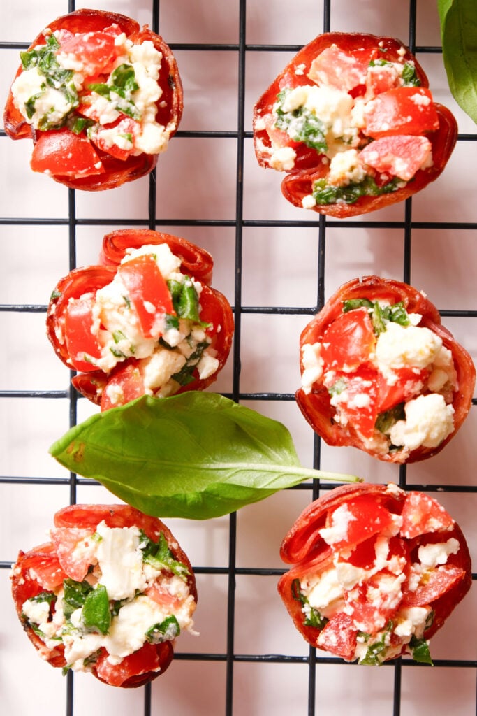 Bouchées de salami croustillantes remplies d'un mélange de tomate, feta et basilic disposées sur une grille de refroidissement avec des feuilles de basilic frais.