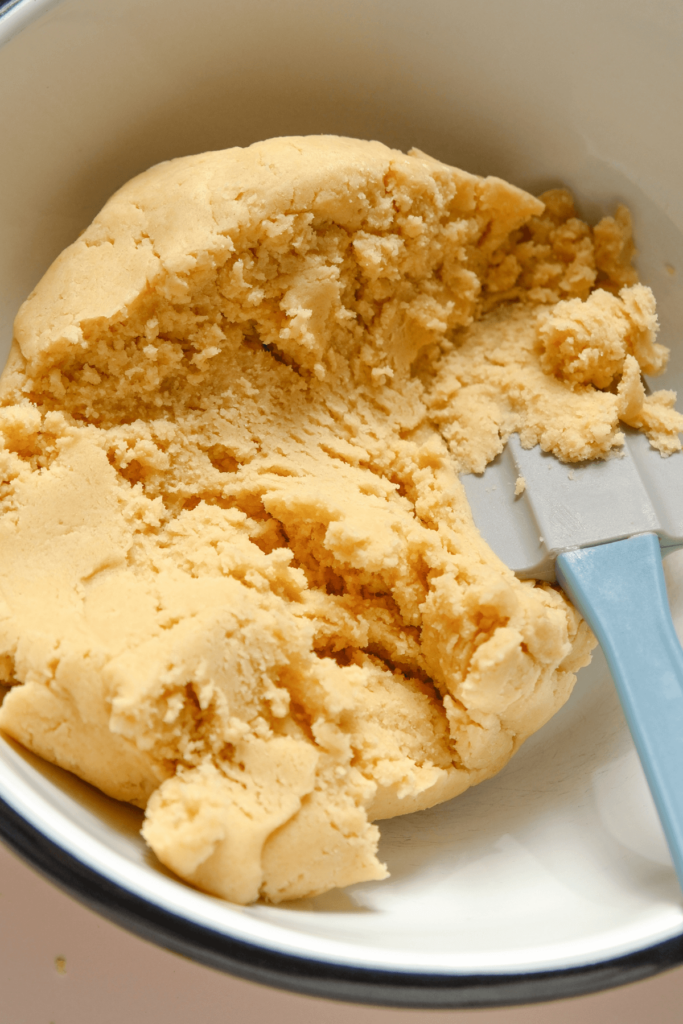 Gros plan sur la pâte à biscuits au sucre lisse dans un bol avec une spatule, prête à être étalée pour la découpe.