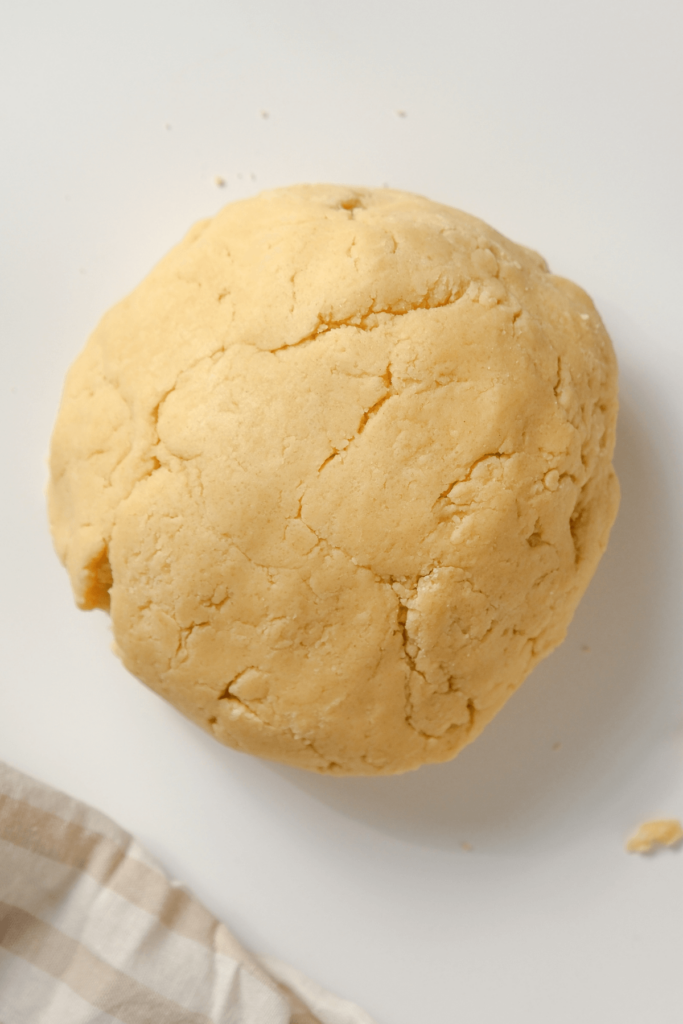 Une boule de pâte à biscuits au sucre lisse reposant sur une surface blanche, prête à être étalée pour découper des formes.