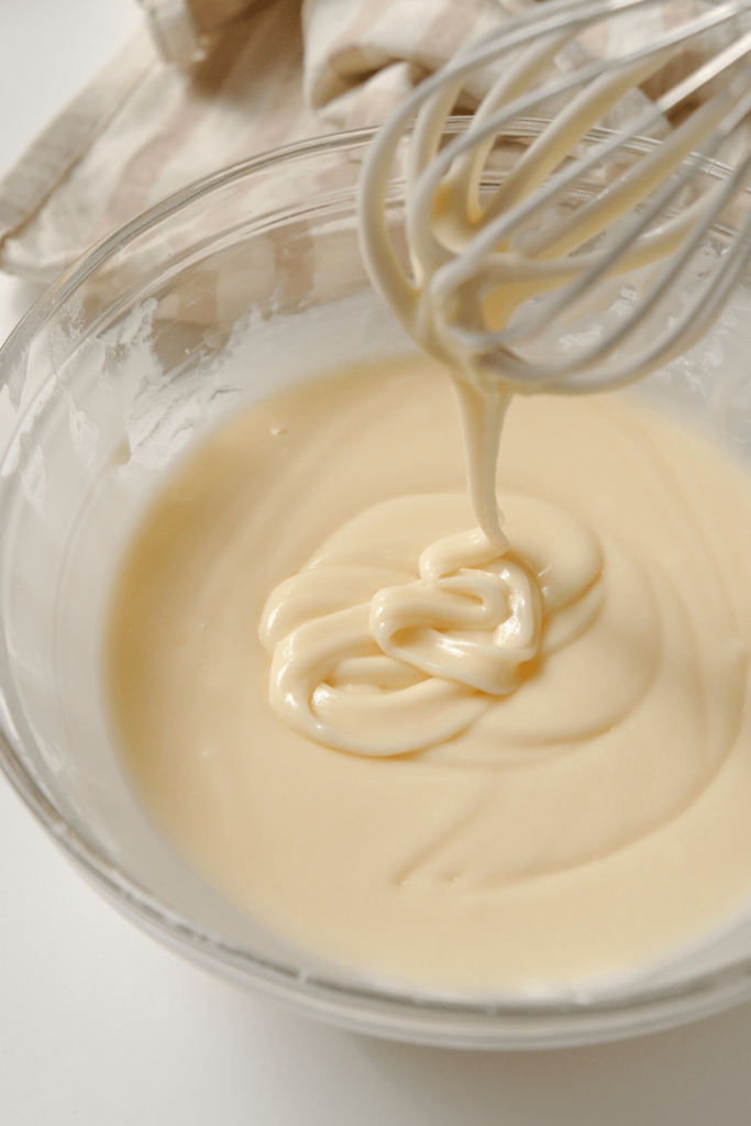 Un bol de glaçage à biscuits au sucre lisse et brillant avec un fouet sorti, montrant la consistance parfaite pour décorer les biscuits au sucre.