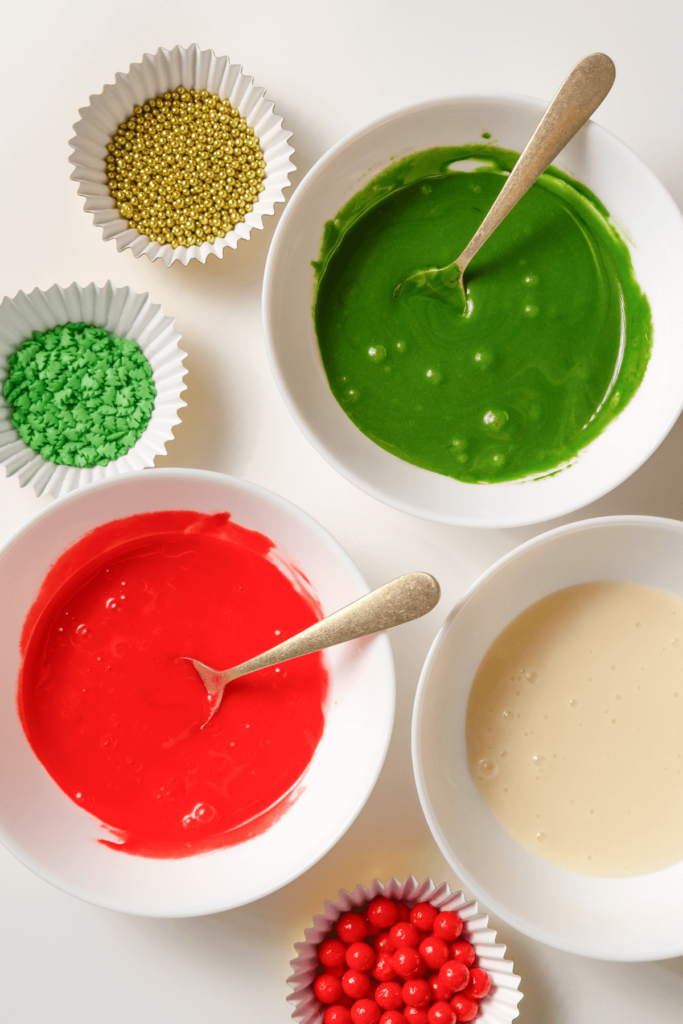 Bols de glaçage rouge, vert et blanc avec des vermicelles dorés, verts et rouges arrangés sur un fond blanc.