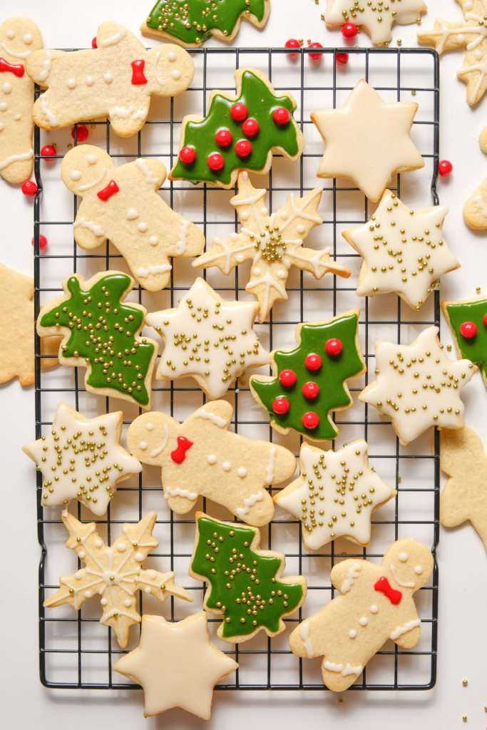 Assortiment de biscuits de Noël décorés, y compris des bonhommes en pain d'épice, des étoiles, des feuilles de houx et des flocons de neige, avec glaçage blanc et vert sur une grille de refroidissement.