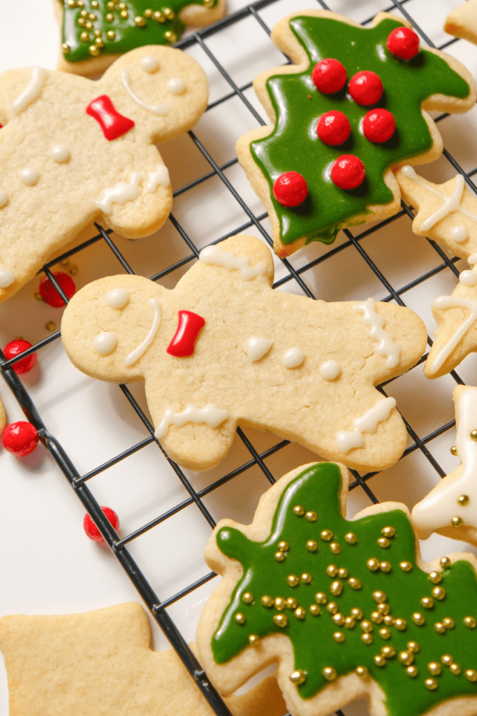 Gros plan sur un bonhomme en pain d'épice et des biscuits en forme de sapin de Noël décorés sur une grille de refroidissement, avec du glaçage rouge et vert et des vermicelles festifs.