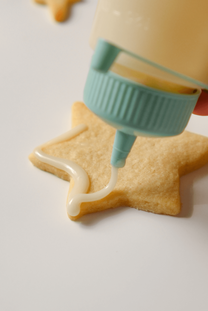 Gros plan sur le glaçage appliqué sur un biscuit de Noël en forme d'étoile à l'aide d'une bouteille en plastique.