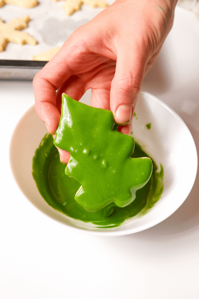 Gros plan sur un biscuit en forme de sapin de Noël étant tenu, couvert d'un glaçage vert vibrant.