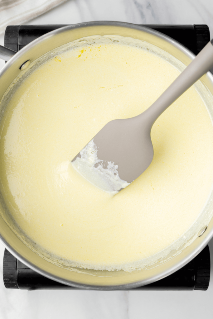 Mélange de beurre fondu et de crème en cours de remuage avec une spatule grise dans une casserole.