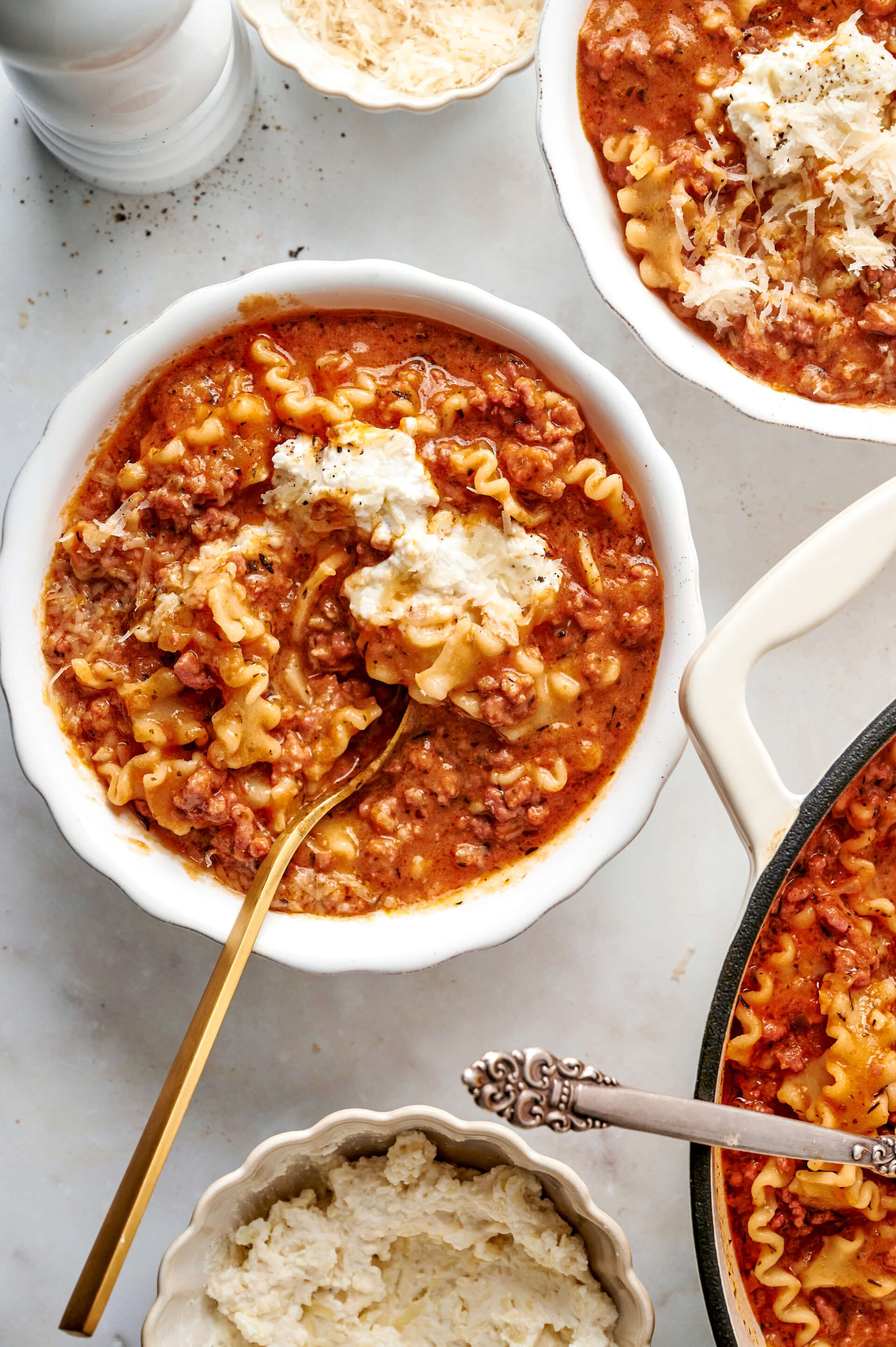 Meilleure Recette de Soupe de Lasagne – Crémeuse, Au Fromage & Confortable Un bol de soupe de lasagne crémeuse avec des nouilles ondulées, un riche bouillon de tomate, du bœuf haché, et une cuillerée de fromage ricotta, servi avec une cuillère dorée.