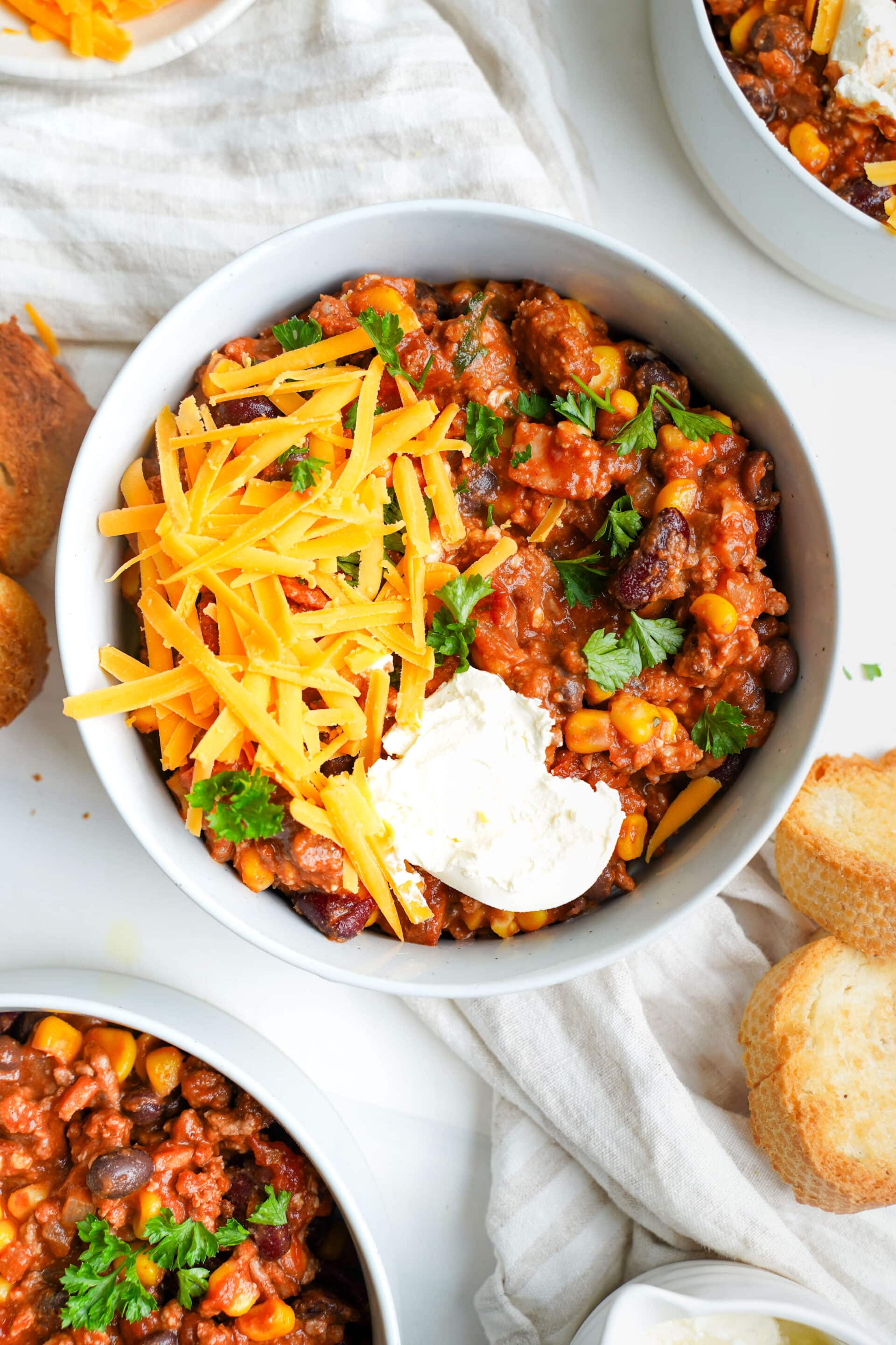 Un bol de chili au boeuf copieux garni de fromage cheddar râpé, de crème aigre et de coriandre fraîche, servi avec des tranches de baguette grillées.