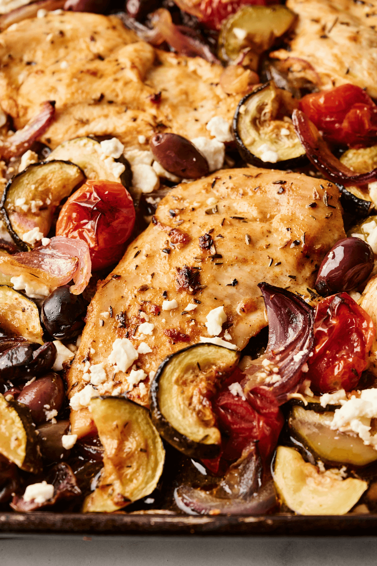 Gros plan du dîner de poulet grec au four avec des légumes rôtis, des olives et du fromage feta.