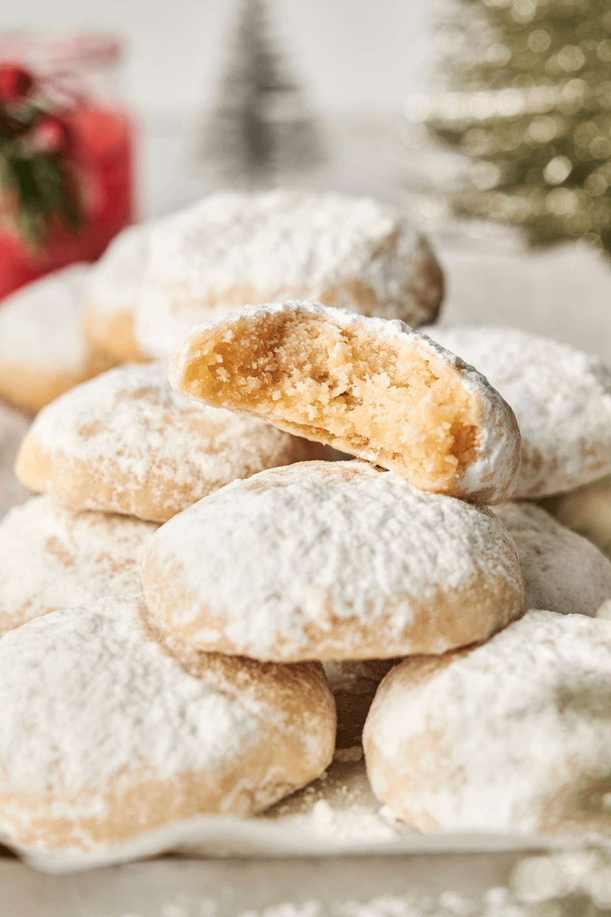 Une pile de biscuits boule neige aux amandes saupoudrés de sucre glace, avec un biscuit cassé en deux pour montrer son intérieur doux et beurré.