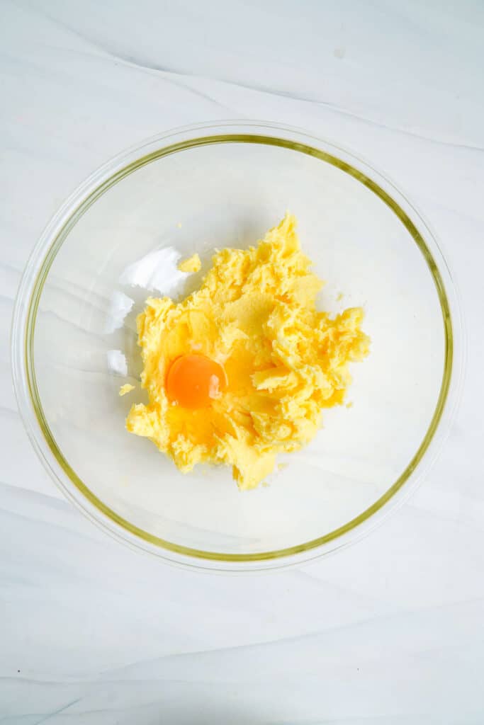 Beurre et sucre crémeux dans un bol en verre avec l'ajout d'un œuf et d'extrait d'amande.