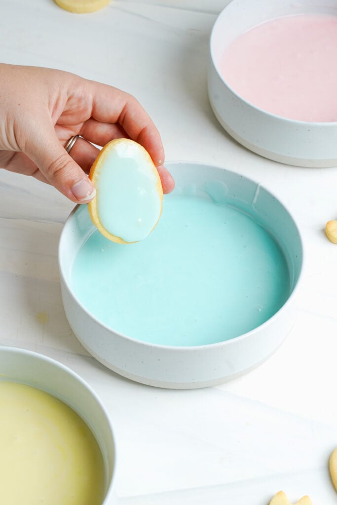 Biscuits de Pâques fraîchement trempés étant levés d'un bol de glaçage bleu pastel avec une couche lisse.