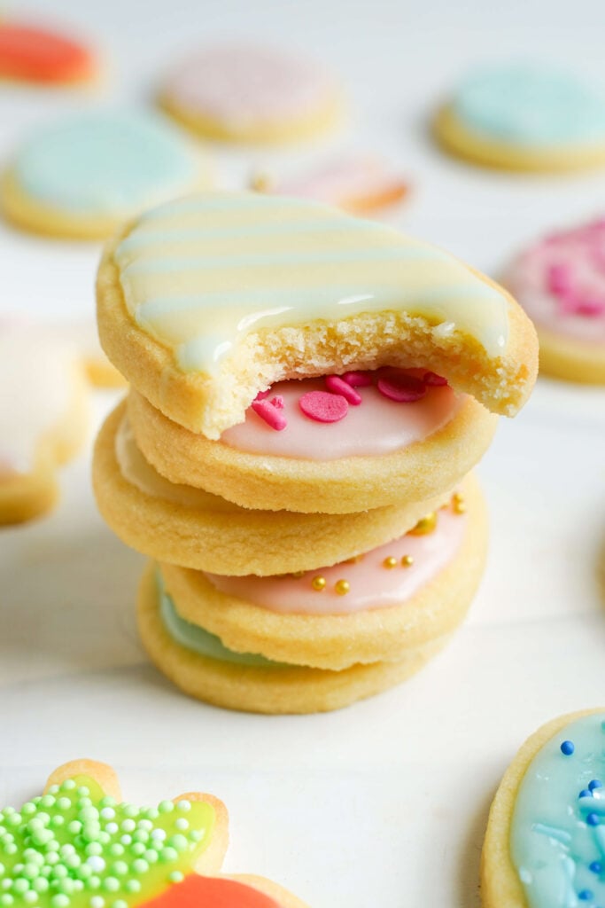 Empilement de biscuits de Pâques décorés avec du glaçage pastel et des vermicelles, avec le biscuit du haut montrant une bouchée pour révéler sa texture douce et tendre.