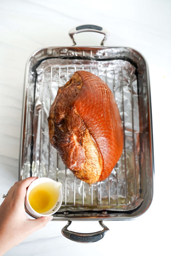Main versant du bouillon de poulet dans un plat de cuisson tapissé de papier aluminium avec un jambon en spirale avant la cuisson