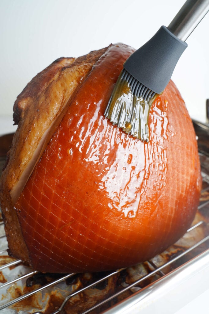 Badigeonnage du glaçage au sucre brun sur le jambon découpé en spirale dans le plat de cuisson