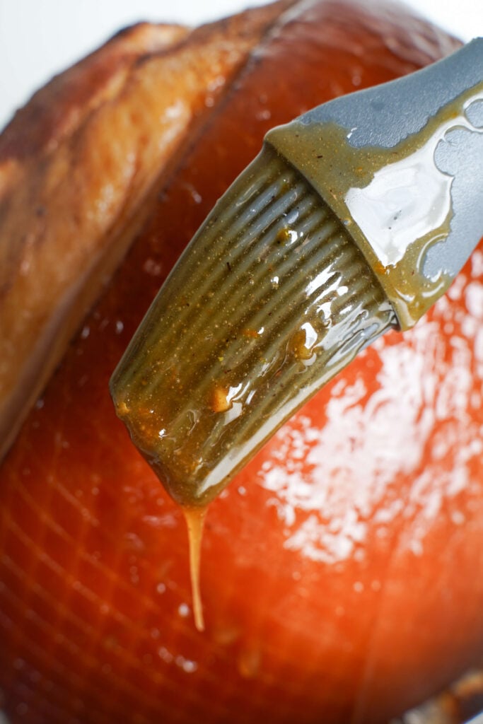 Pinceau en silicone avec glaçage collant au sucre brun recouvrant le jambon en spirale
