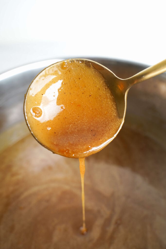 Cuillère laissant tomber le glaçage au sucre brun chaud avec des éclats d'épices sur une casserole