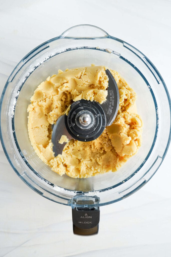 Pâte de croûte de sablé dans un robot culinaire, juste combinée et formant une texture douce et granuleuse.