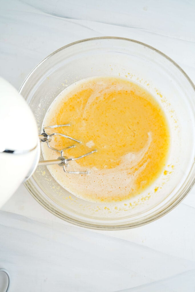 Garniture lisse pour barres au citron dans un bol en verre, en cours de mélange avec un batteur à main jusqu'à ce qu'elle soit complètement combinée et légèrement mousseuse.