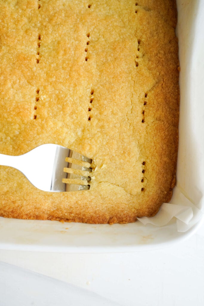 Utilisation d'une fourchette pour piquer doucement des trous dans la croûte de sablé fraîchement cuite pour aider la garniture au citron à adhérer.