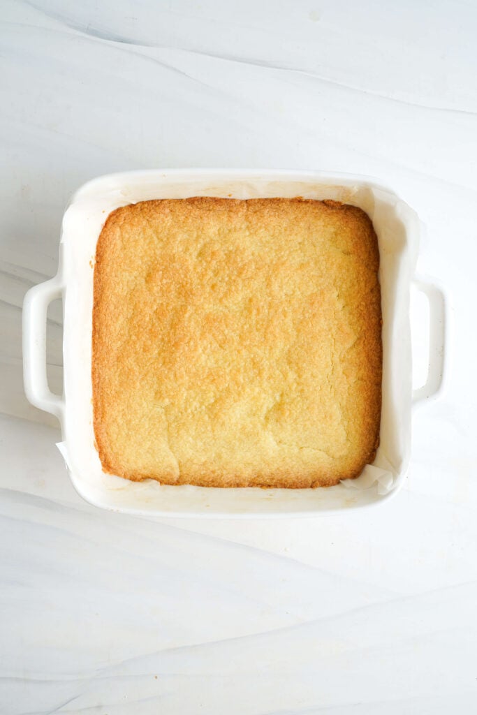 Croûte de sablé dorée juste sortie du four, refroidissant dans un moule tapissé de papier sulfurisé avant que la garniture au citron soit versée sur le dessus.