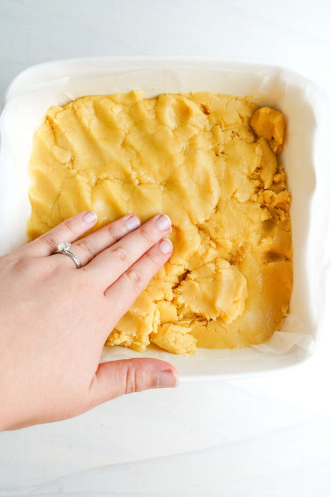 Main pressant la pâte de croûte de sablé uniformément dans un plat de cuisson tapissé de papier sulfurisé pour les barres au citron.