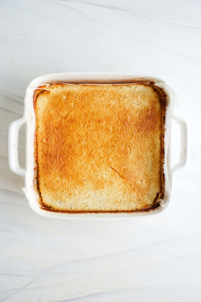Barres au citron dorées venant de sortir du four dans un plat de cuisson blanc, montrant un dessus parfaitement pris et uniformément cuit.