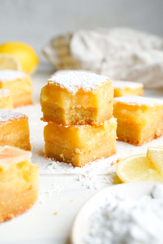 Deux barres au citron épaisses empilées l'une sur l'autre, saupoudrées de sucre glace, avec une bouchée enlevée pour montrer la garniture au citron douce et acidulée et la croûte beurrée.