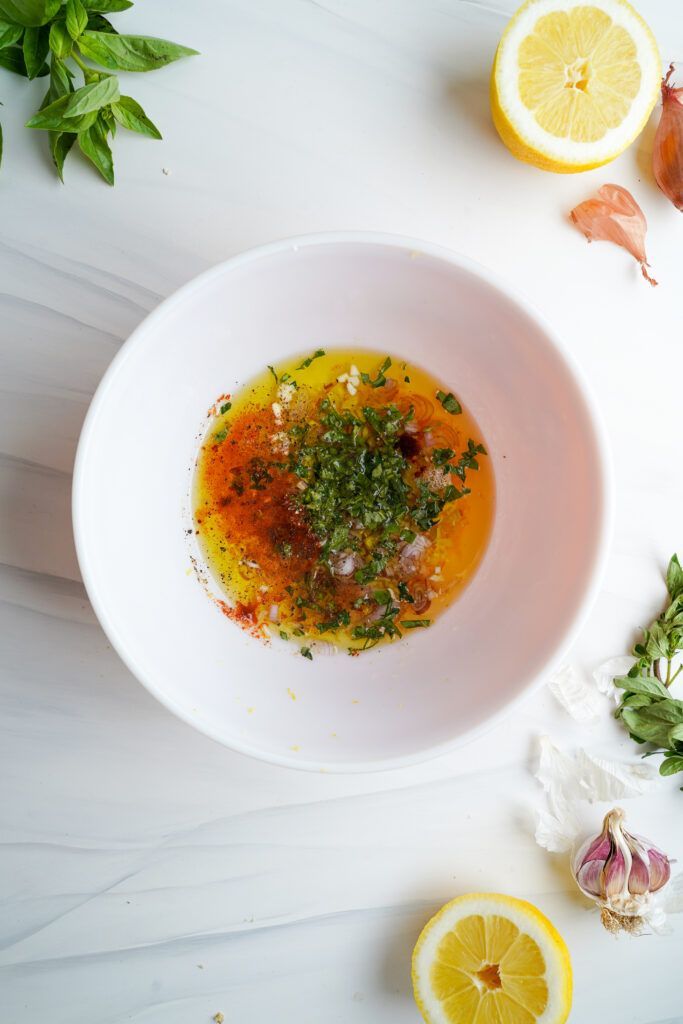 Un mélange d'huile d'olive, de jus de citron, de zeste de citron, de paprika, d'origan, de basilic, d'ail, d'échalote, de sel et de poivre dans un bol